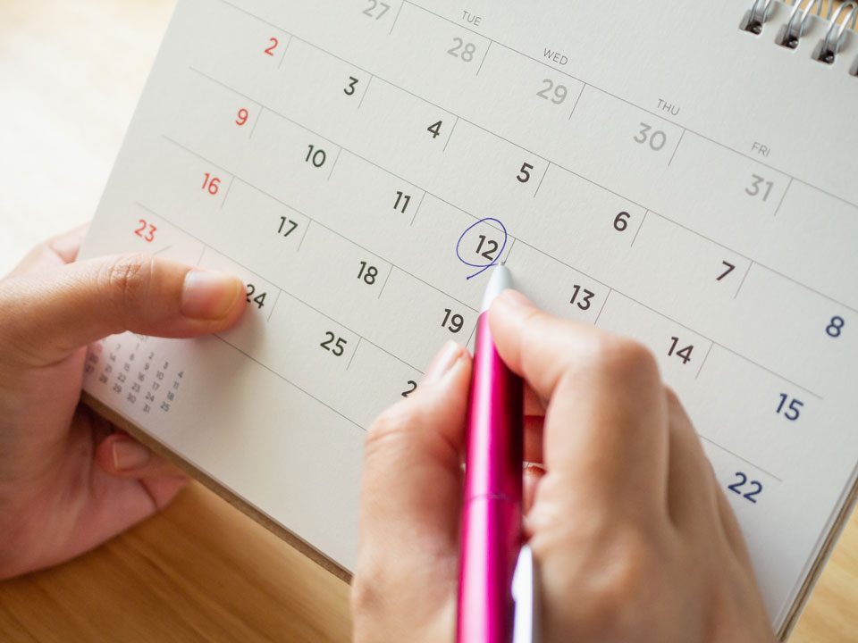 Eine Hand mit Kuli kreist ein Datum auf einem Kalender ein.